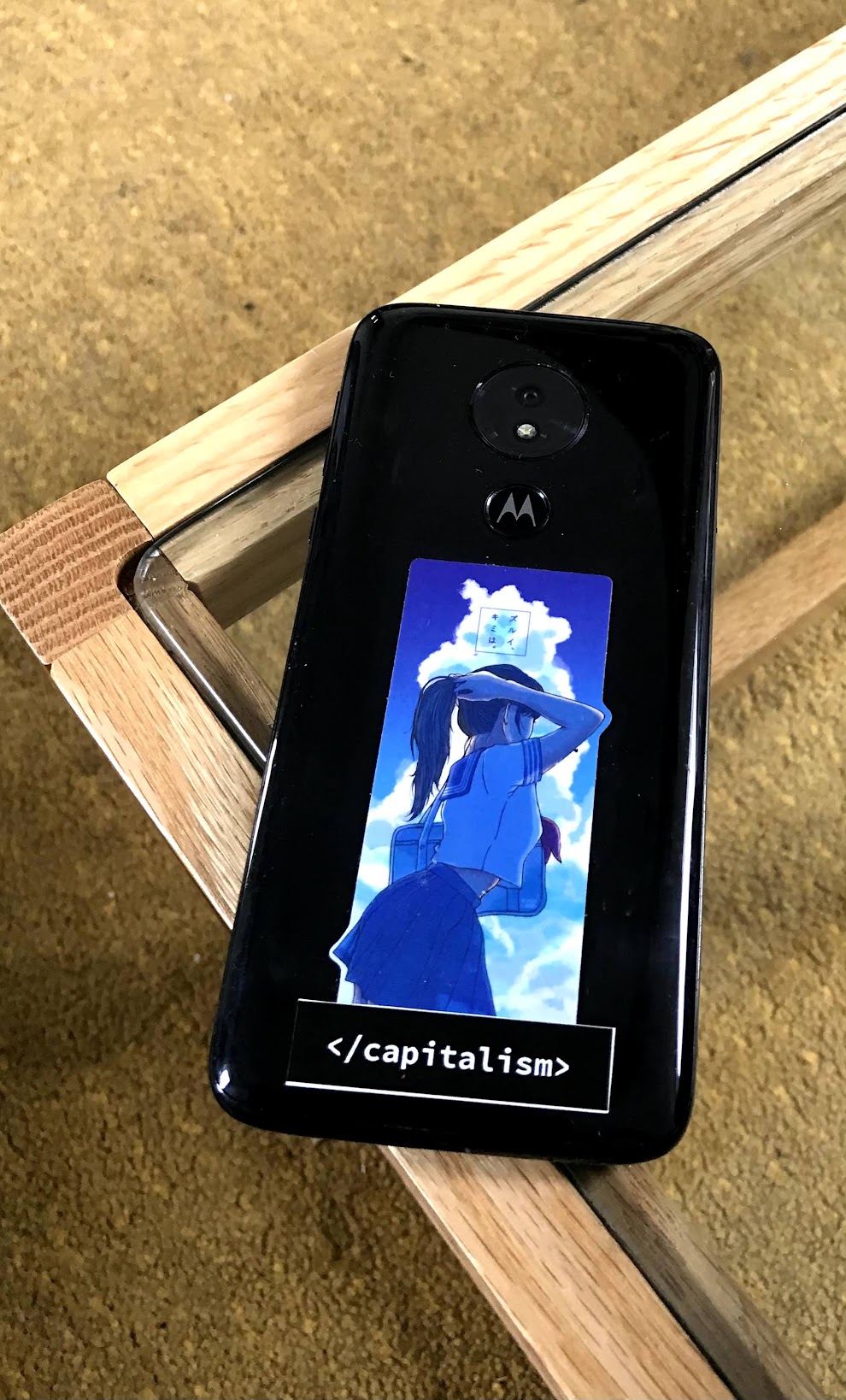 Foto meines Smartphones auf dem ein Anime Aufkleber, sowie der Schriftzug End Capitalism klebt.